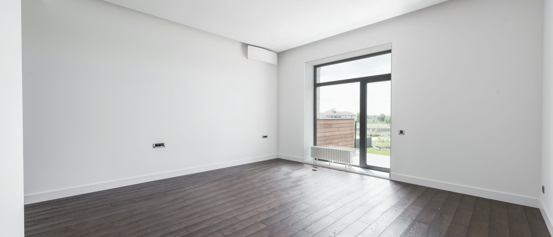 Boş bir dairede balkon kapısından gün ışığı; beyaz duvarlar ve ahşap parke.